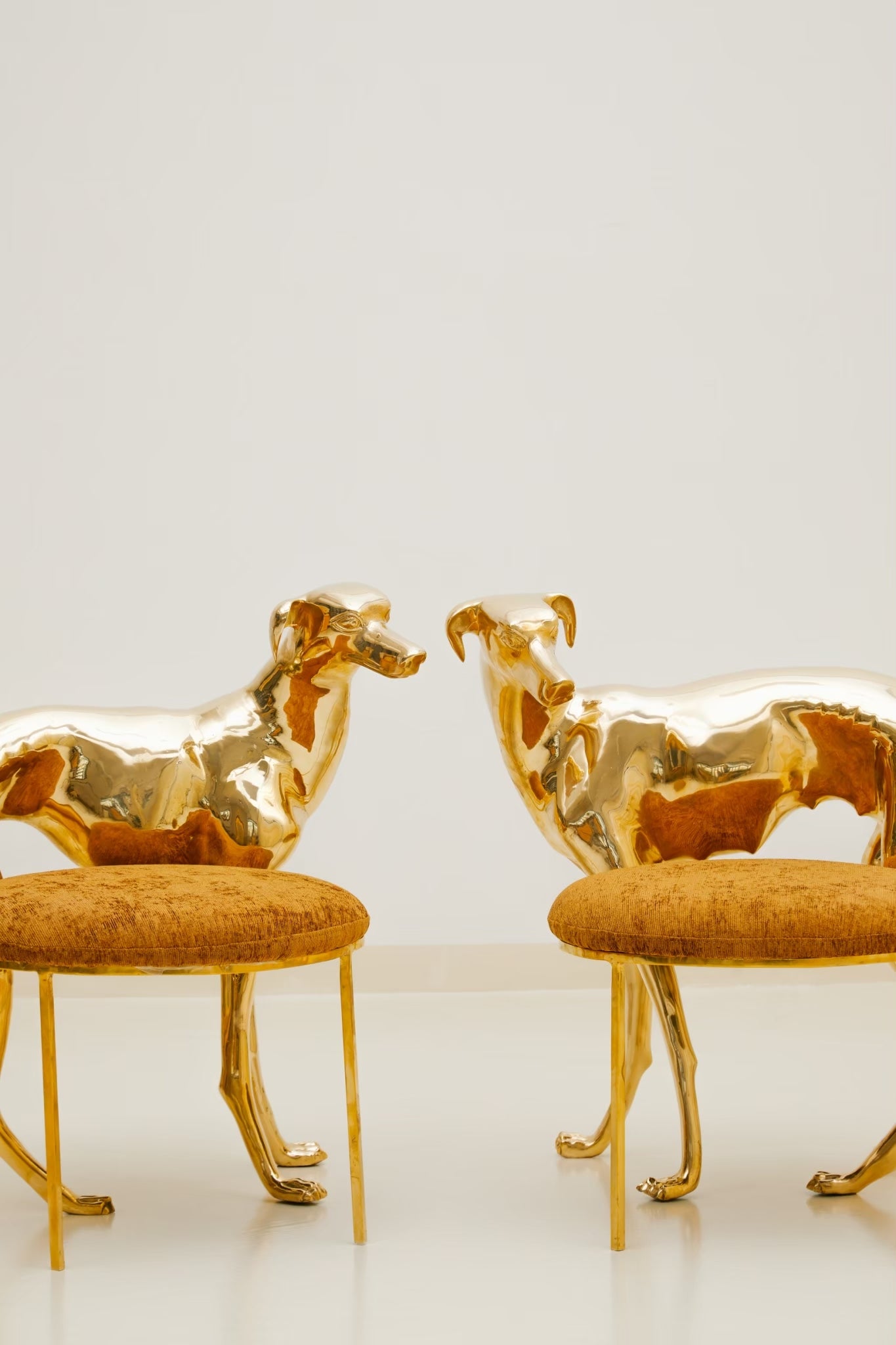 Two gold brass luxury handmade furniture dog-shaped chairs with cushioned seats, ideal for modern luxury decor, on a white background.