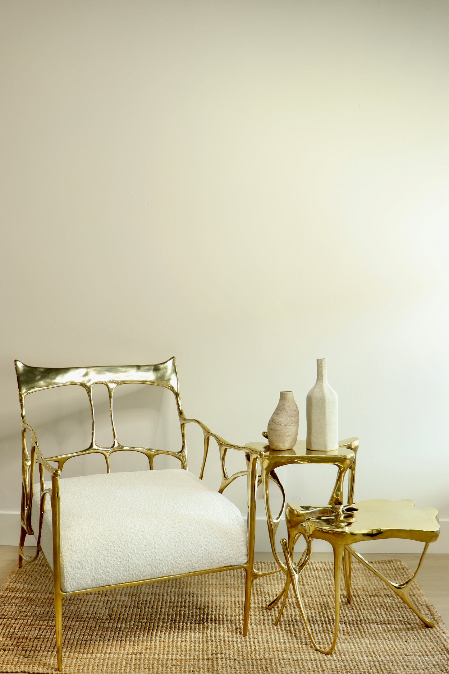 Gold brass luxury handmade furniture chair with two gold brass side tables, styled with vases, perfect for modern luxury decor, on a beige background.