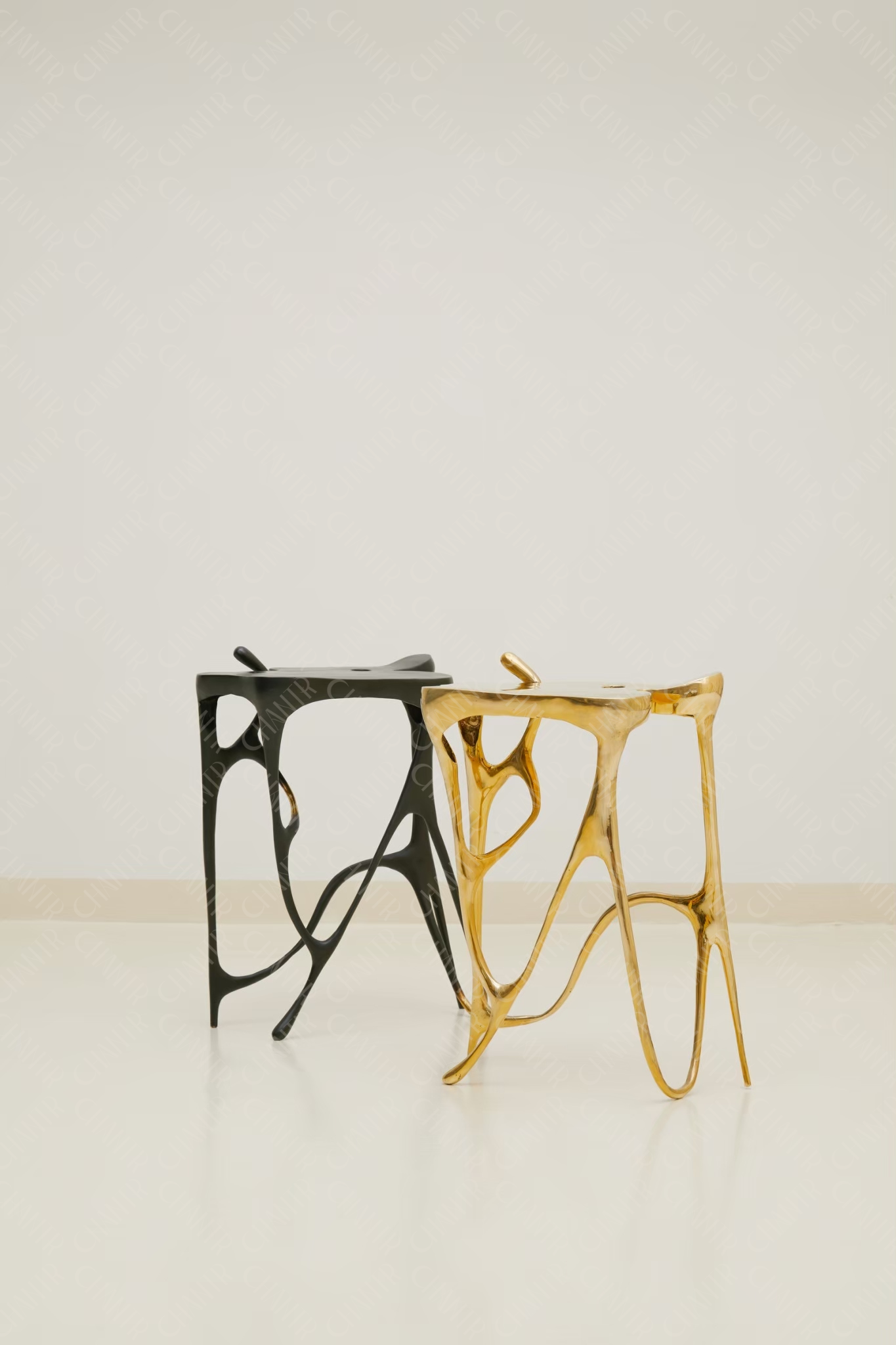 Two luxury handmade furniture taller stools, one gold brass and one black, designed for modern luxury decor, on a white background.