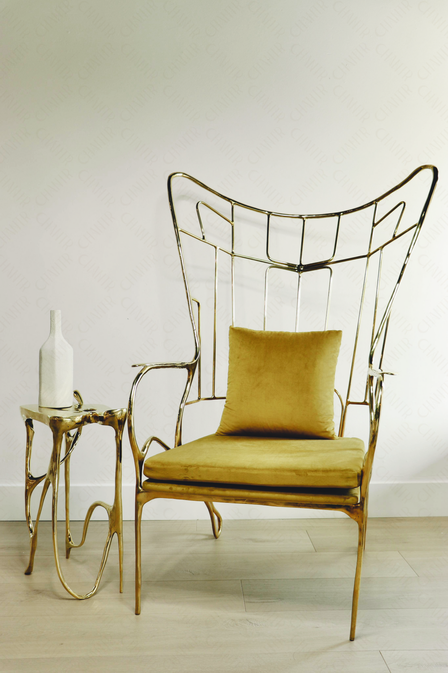 Gold brass luxury handmade furniture chair with cushion on a light wooden floor, paired with a gold brass side table topped with a white vase, perfect for modern luxury decor.