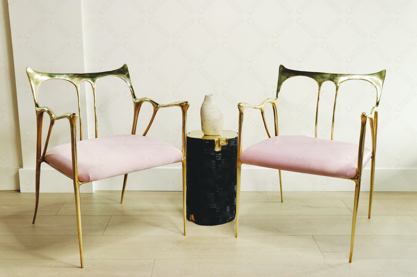 Two gold brass luxury handmade furniture chairs with pink cushions flanking a black and gold brass stool with a vase, perfect for modern luxury decor.
