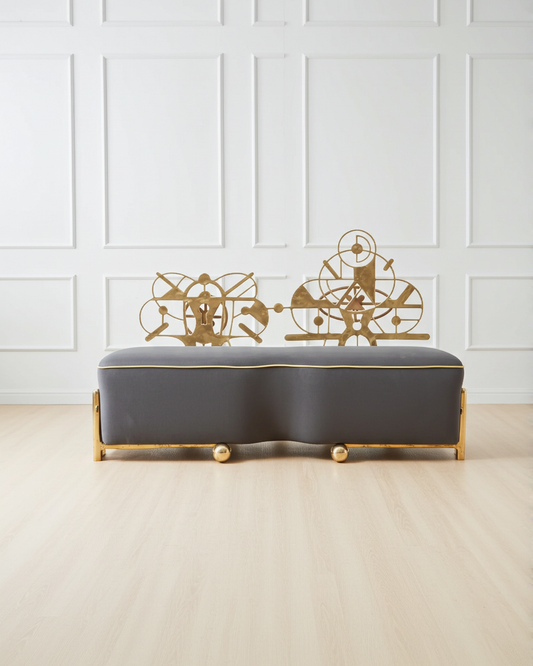 Gray bench with gold brass decorative elements against a white paneled wall.