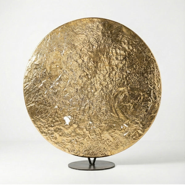 Gold circular sculpture on a stand against a white background