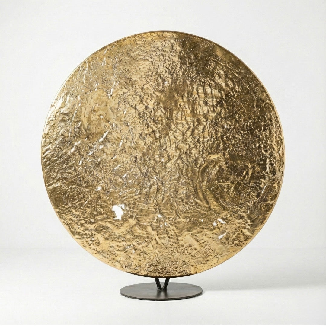 Gold circular sculpture on a stand against a white background