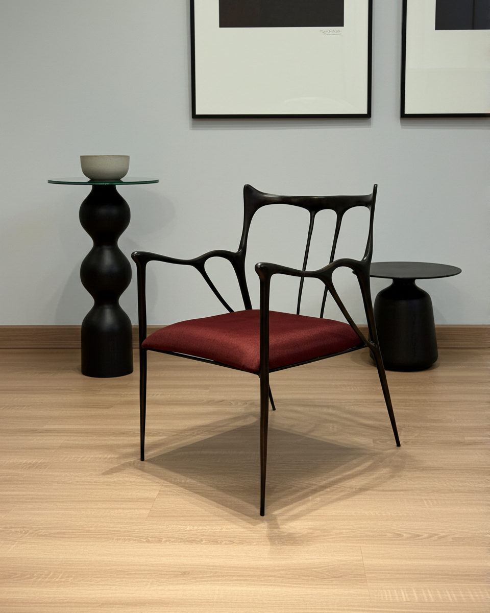 luxury handmade black brass chair with red cushion in a minimalistic room with black side tables and framed art on the wall.