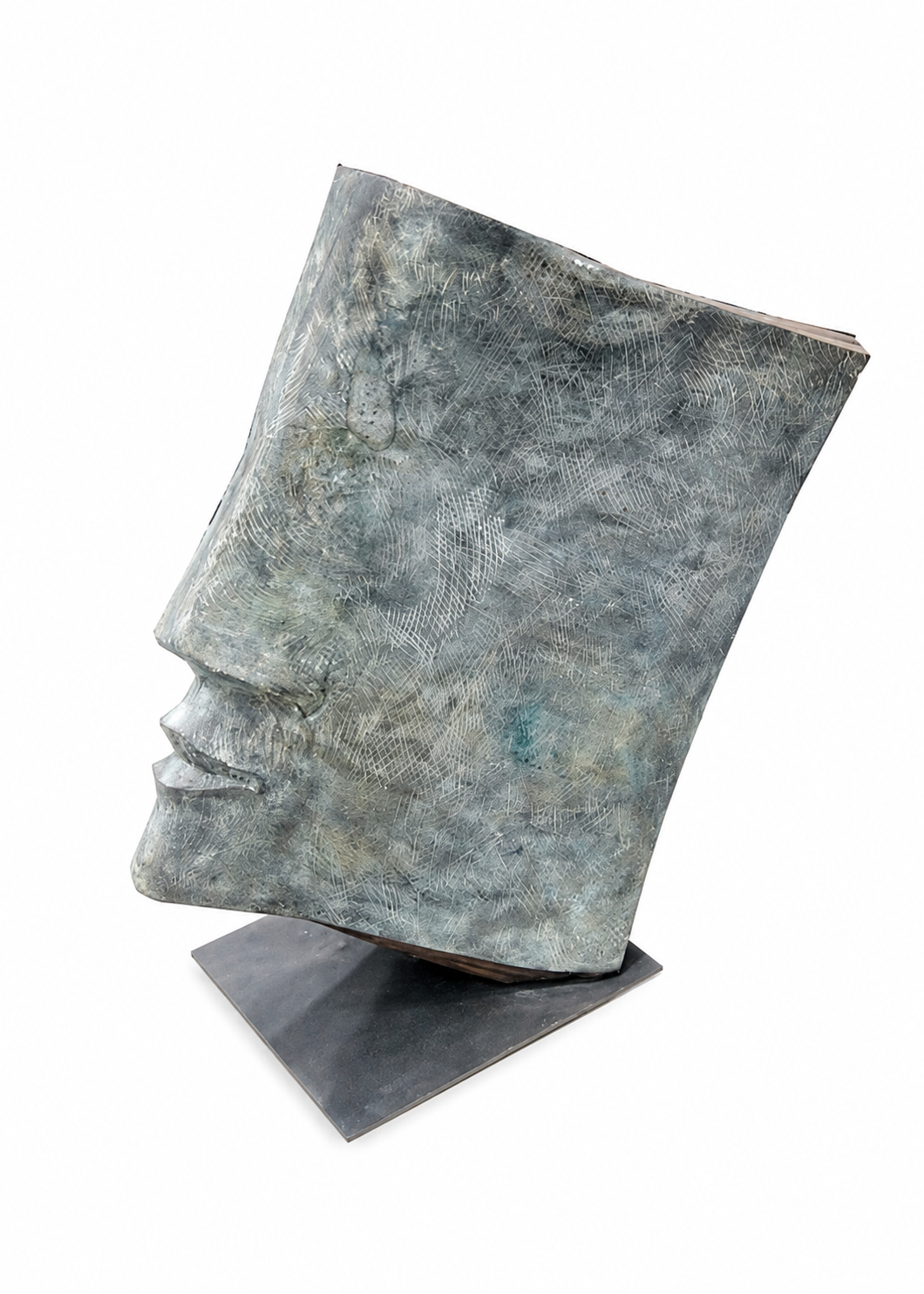 A bronze textured, sculptural book-shaped object with a metallic finish in muted blue-gray tones, displayed on a dark rectangular base against a clean white background.