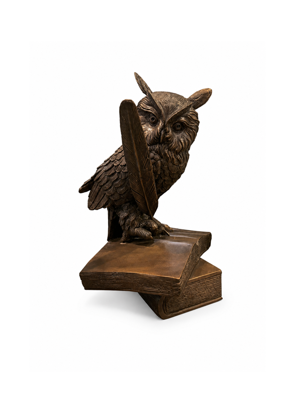 A bronze owl sculpture perched on two stacked books, holding a large feather in its beak, photographed against a plain white background.