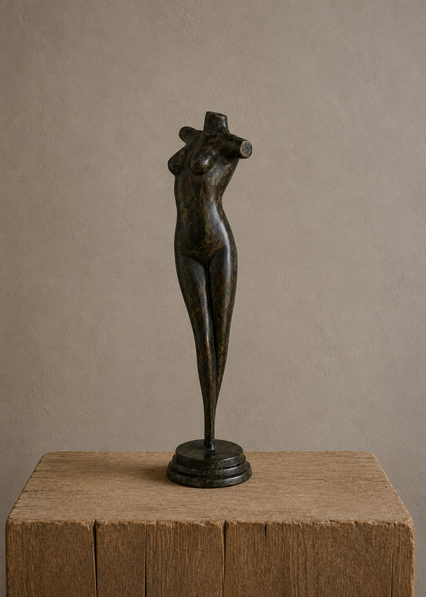A dark bronze sculpture of a stylized female torso on a round base, displayed on a rustic wooden block against a neutral beige background.