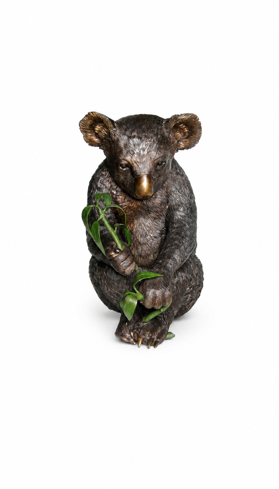 A koala bronze figurine posed sitting and holding green leaves, photographed against a plain white background.