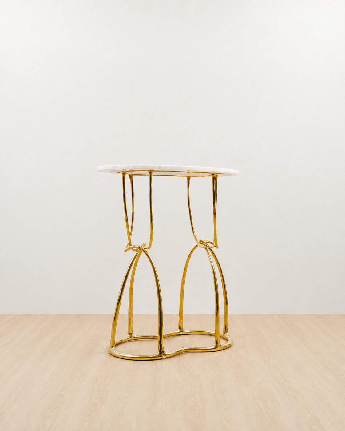 A modern console table featuring a polished gold brass frame and a white marble top, set against a minimalist white wall and light wood floor.