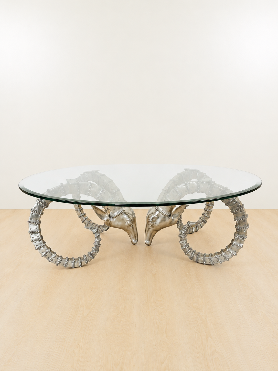 Glass-top coffee table with silver ram-head base and circular horns
