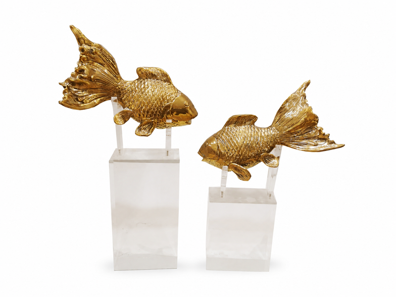 Two gold fish sculptures on clear stands against a white background