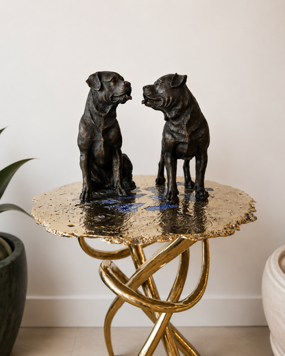 Bronze dog statues on a gold side table against a white wall.