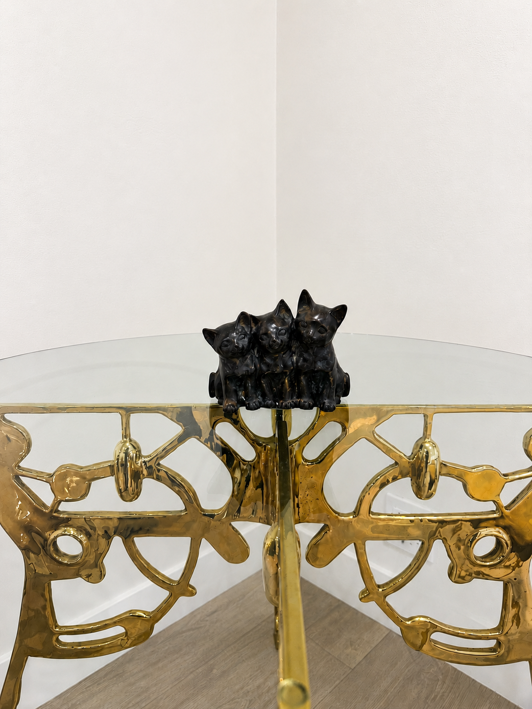 Decorative table with gold base and glass top, featuring a black cat figurine.
