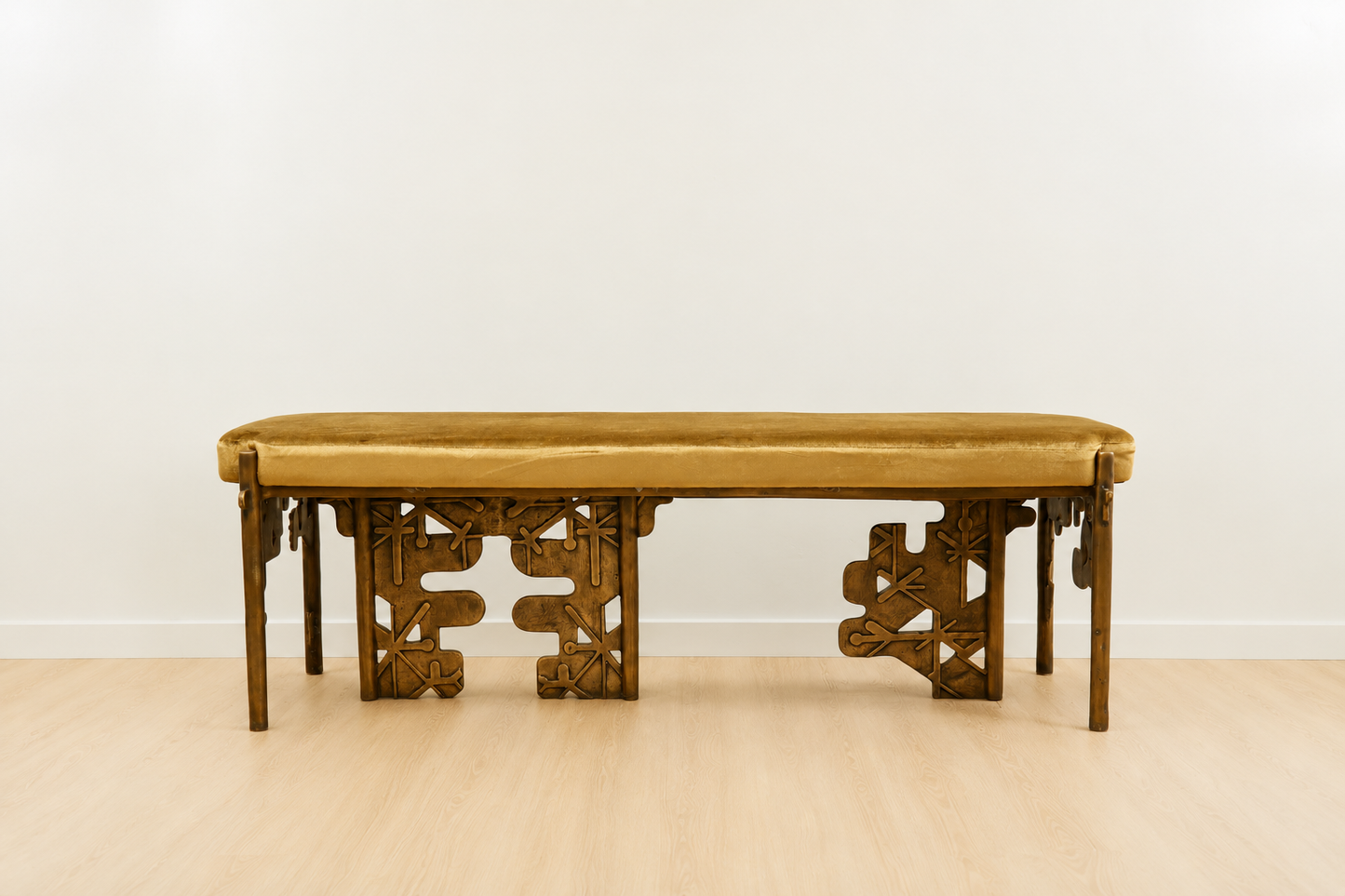 brass bench with intricate carvings with a yellow velvet cushion on a plain background