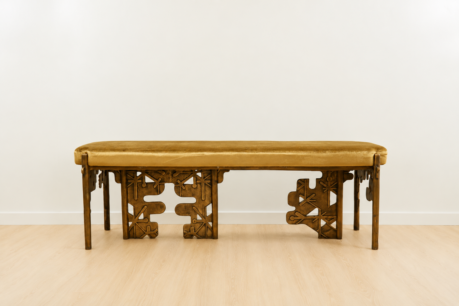 brass bench with intricate carvings with a yellow velvet cushion on a plain background