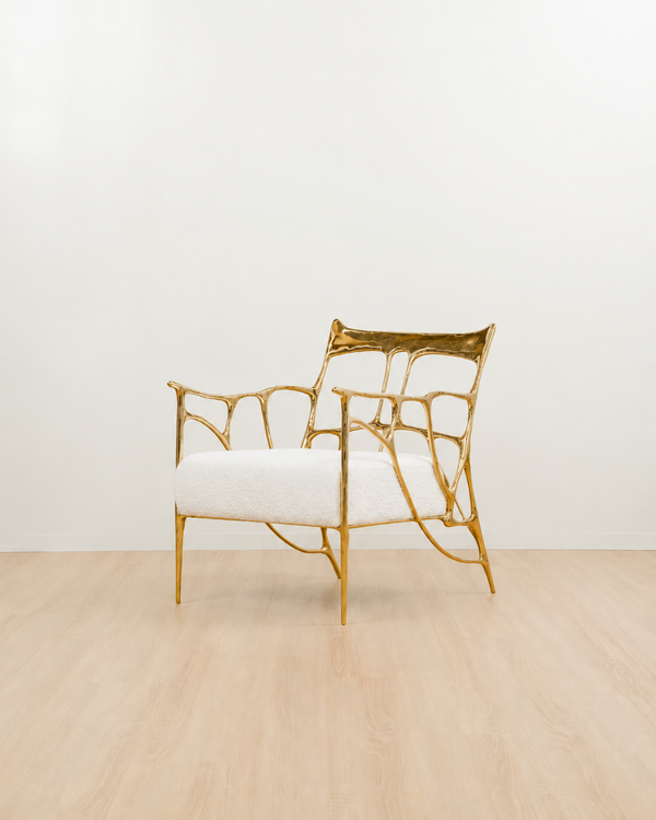 gold, polished brass armchair with white cushion on a light wooden floor. side view