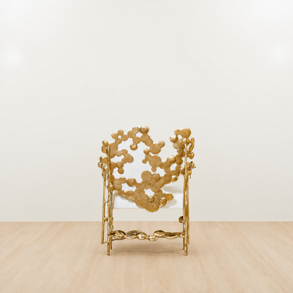 gold brass polished chair with white cushion on a beige floor and light beige wall. back view.