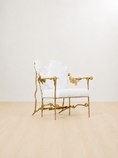 gold brass polished chair with white cushion on a beige floor and light beige wall. side view.