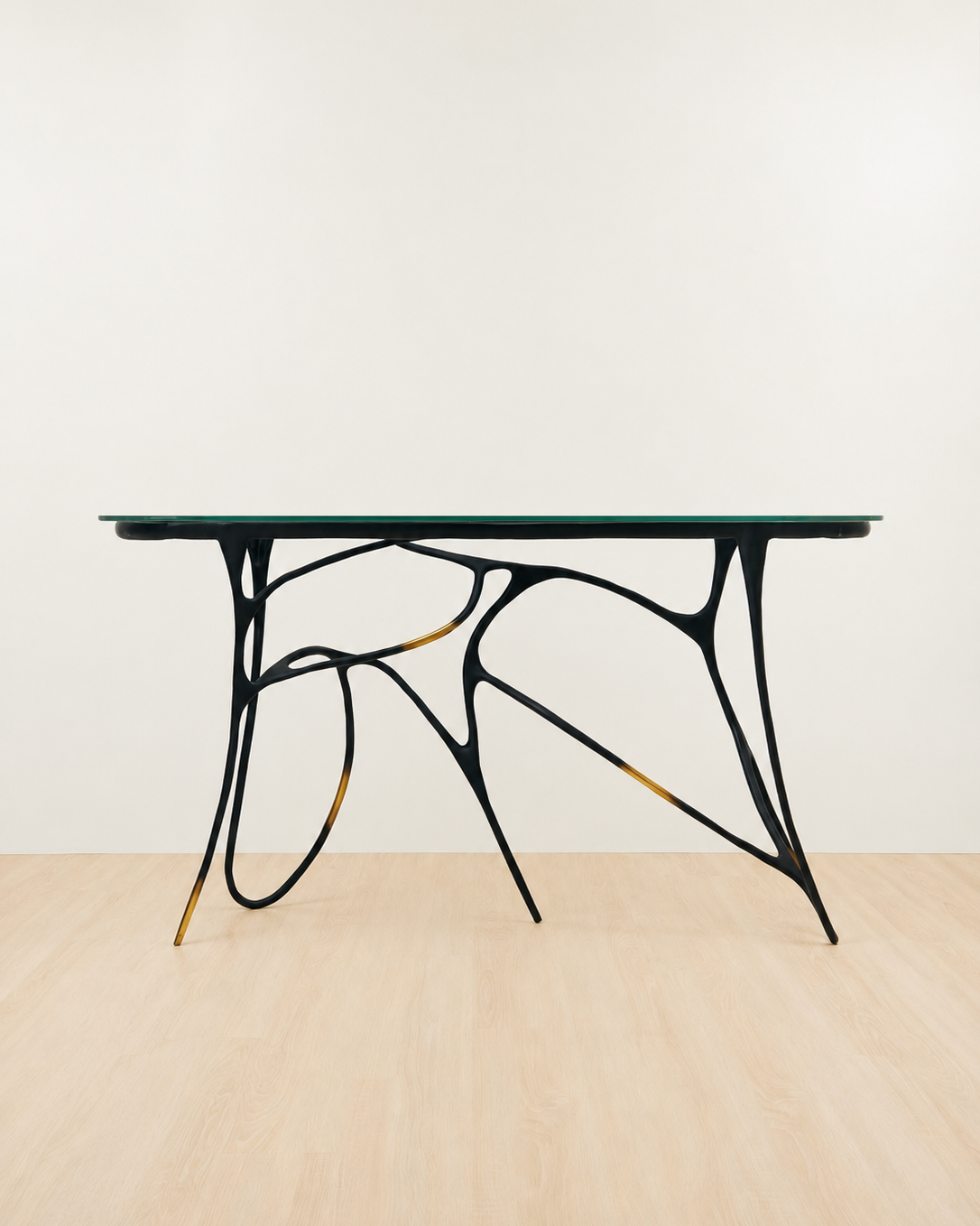 Modern brass console  table with black metal legs and glass top on a beige floor and white wall background