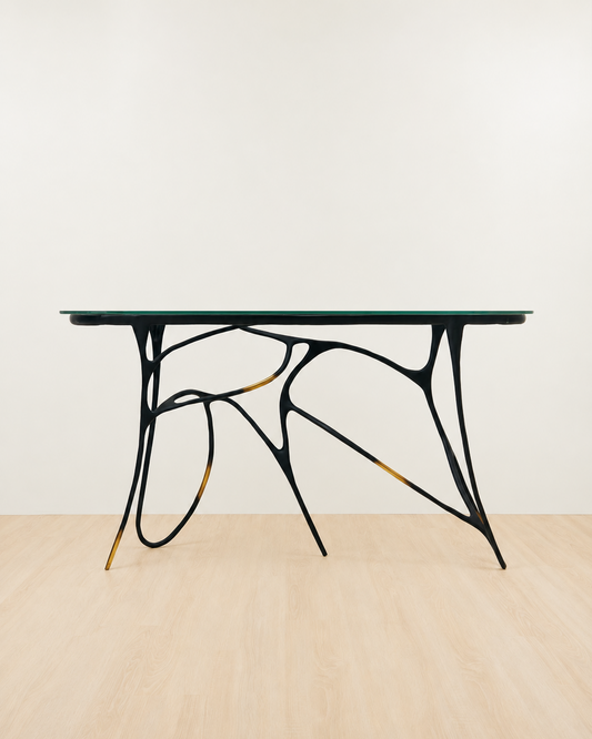Modern brass console  table with black metal legs and glass top on a beige floor and white wall background