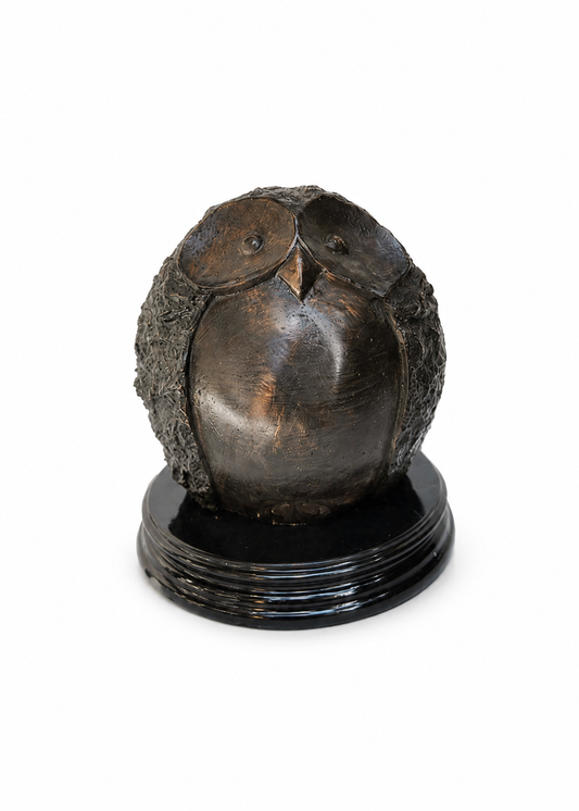 A dark bronze owl sculpture with textured feathers, mounted on a round black base, photographed against a plain white background.