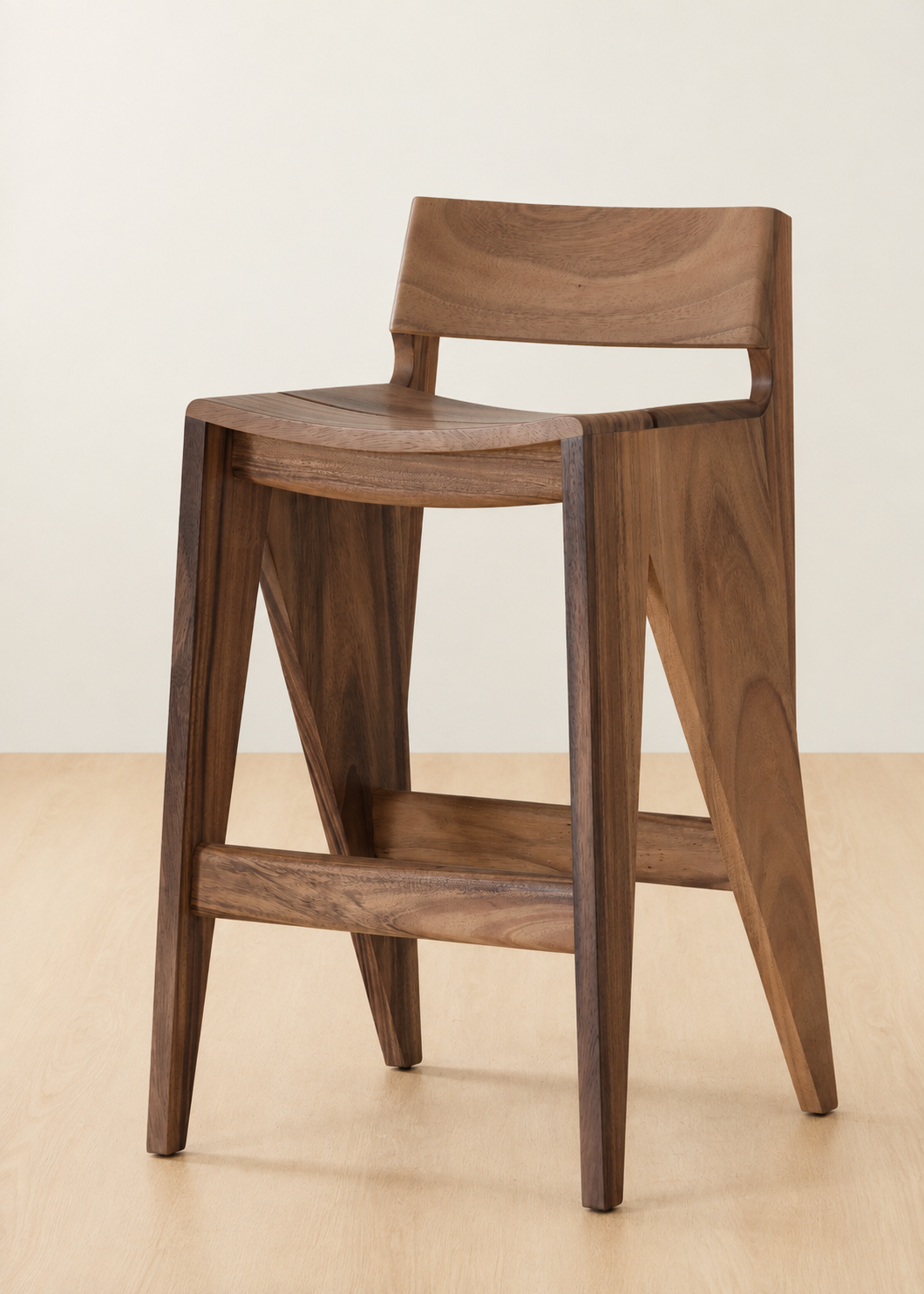 A modern wooden bar stool with a curved seat, backrest, and angled legs, shown on a light wood floor against a plain off-white wall.