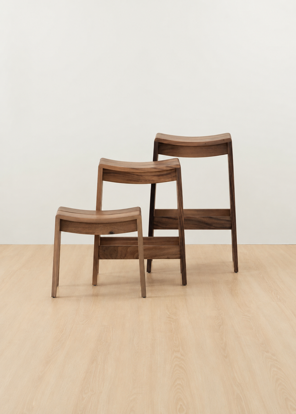 Three wooden chairs of different heights arranged in a row against a plain off-white wall and light wood floor.
