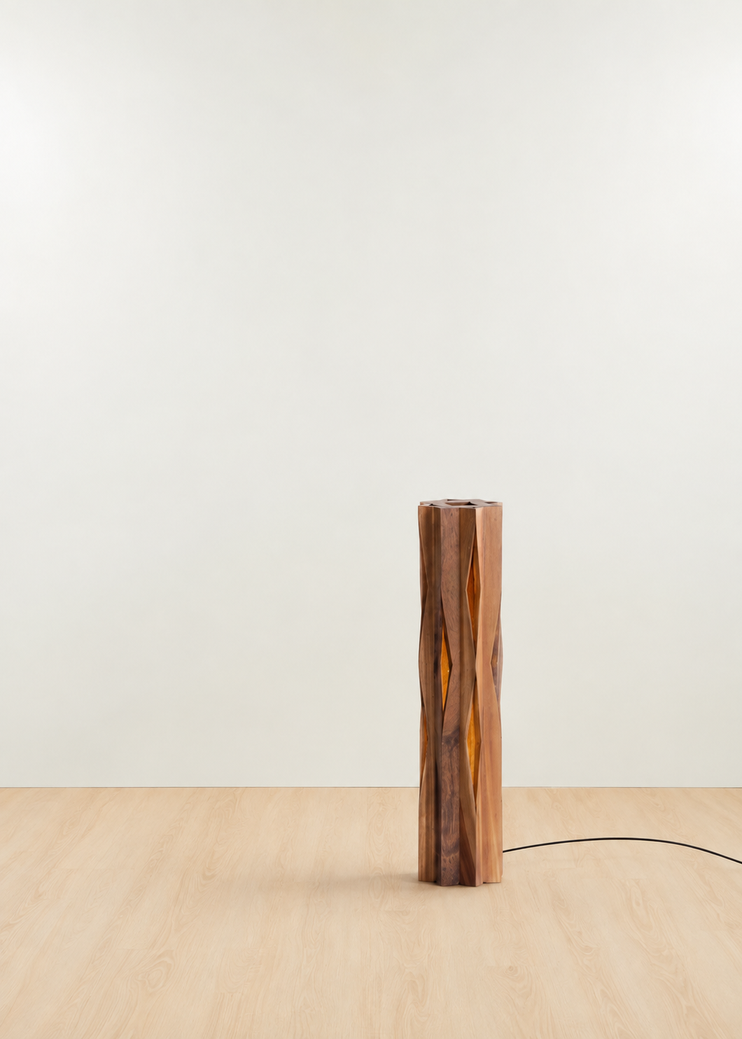 A modern cylindrical table lamp made of polished wood with natural grain patterns, standing on a light wood floor against a plain off-white wall.