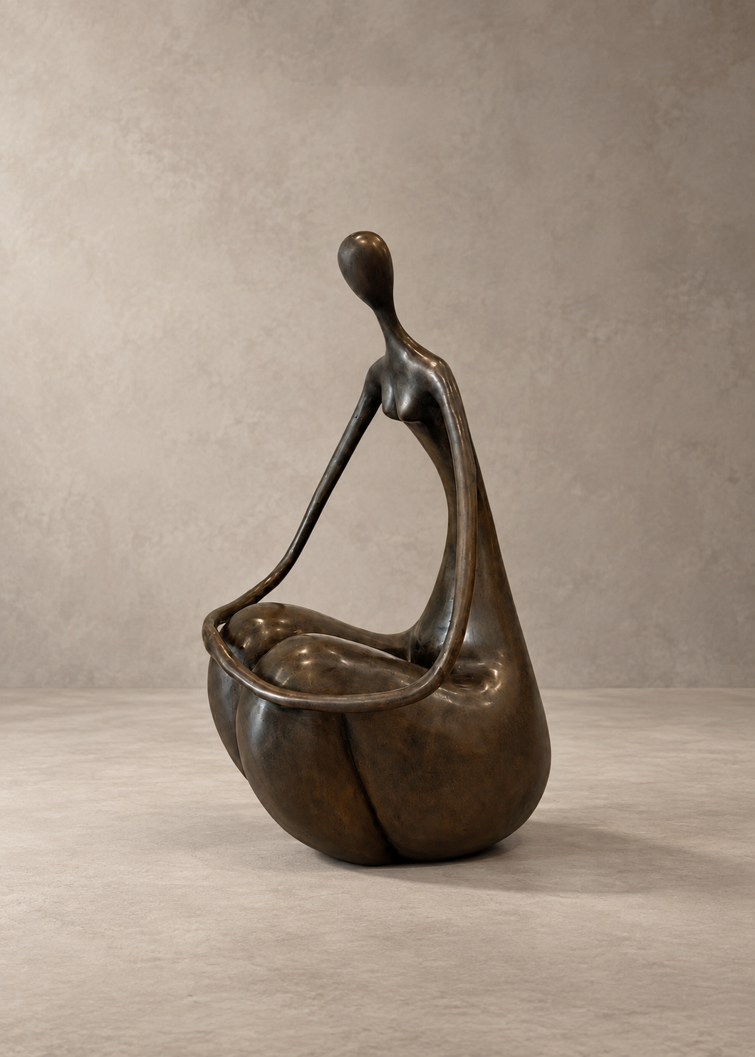 A bronze abstract sculpture of a stylized seated figure holding a rounded basket or vessel, photographed against a neutral textured gray studio backdrop.