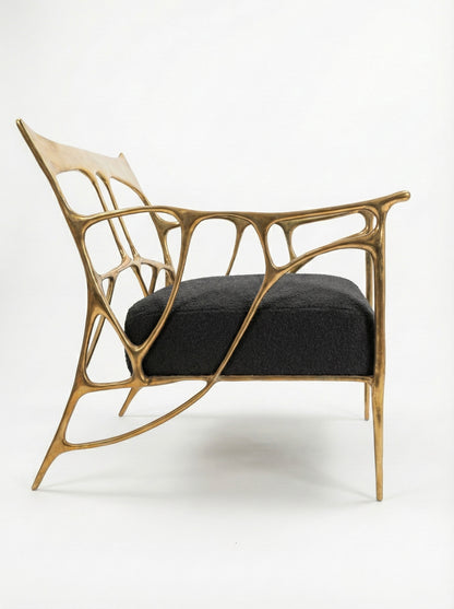 Modern brass chair with gold frame and black cushion on a white background