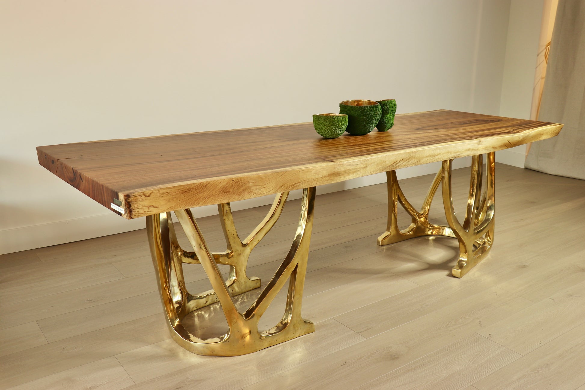 Wooden table top with gold metal legs on a light wooden floor.