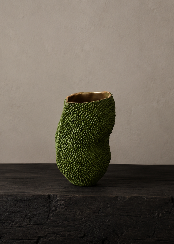 A textured green ceramic vase with a ribbed, bumpy surface and a natural wood-toned interior, displayed on a dark wooden pedestal against a neutral beige plaster wall.