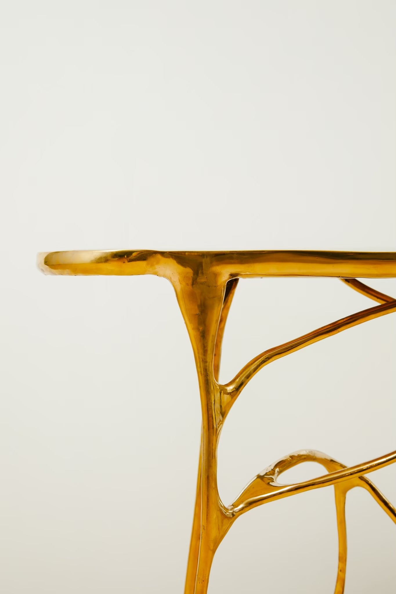 A close-up of a glossy gold metallic table leg with organic, branch-like curves against a plain off-white background.