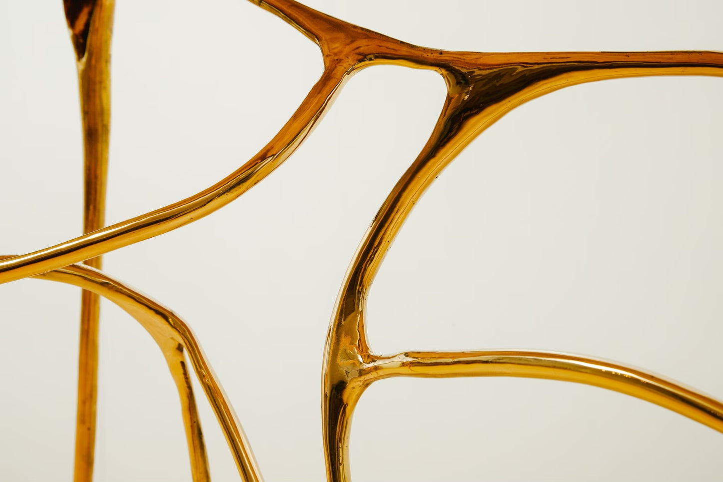 Close-up of a glossy metallic gold abstract sculptural console table structure against a plain light background.