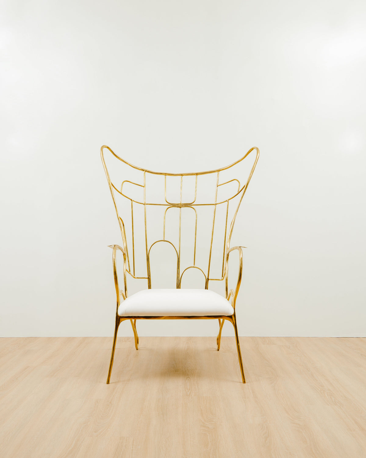 Gold brass chair with white cushion on a light wooden floor,