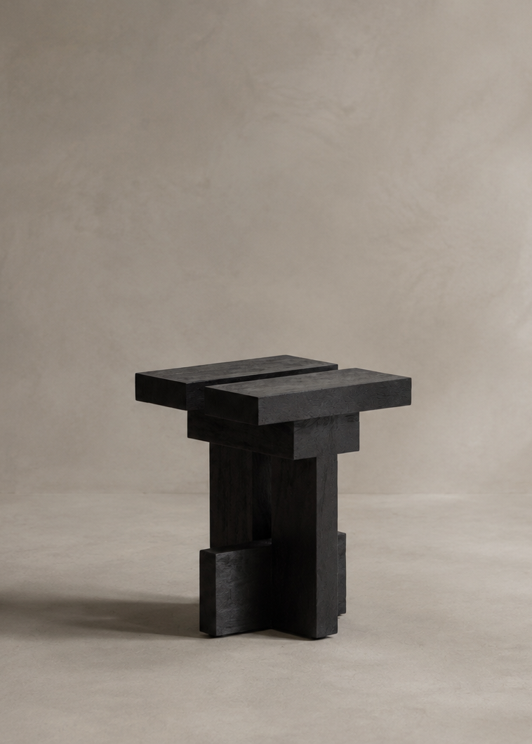 A modern black wooden stool with a geometric, stacked-block design, set against a minimalist textured gray concrete background.