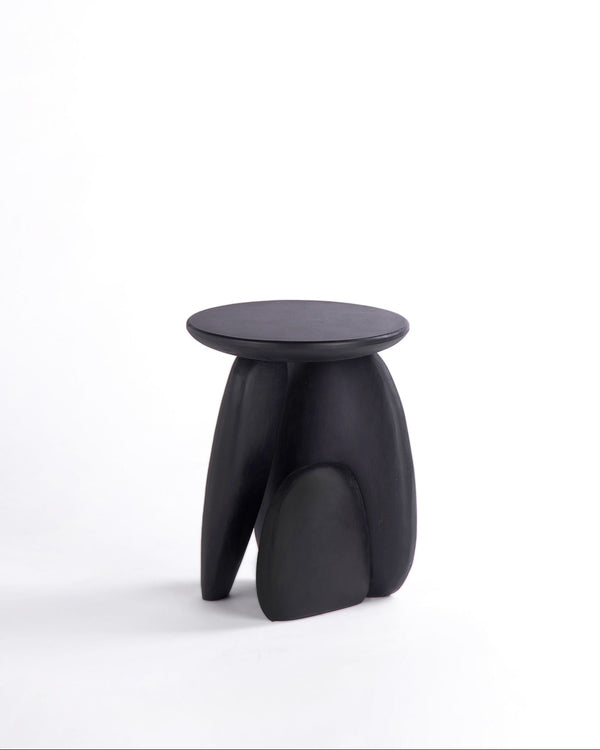 Pebble stool. A minimalist black sculptural stool with a round top and three organic-shaped legs, photographed on a seamless white studio background.