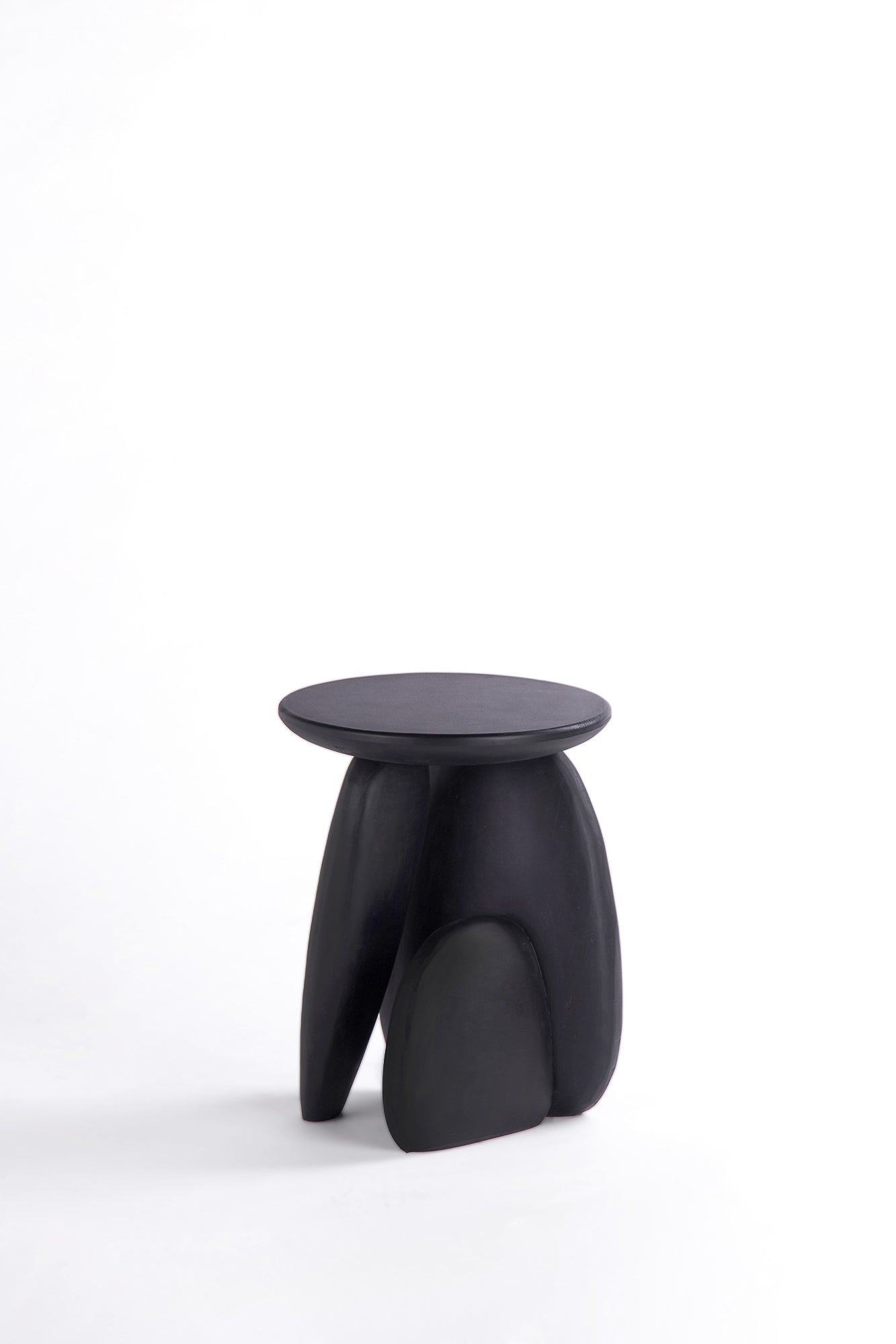 Pebble stool. A minimalist black sculptural stool with a round top and three organic-shaped legs, photographed on a seamless white studio background.