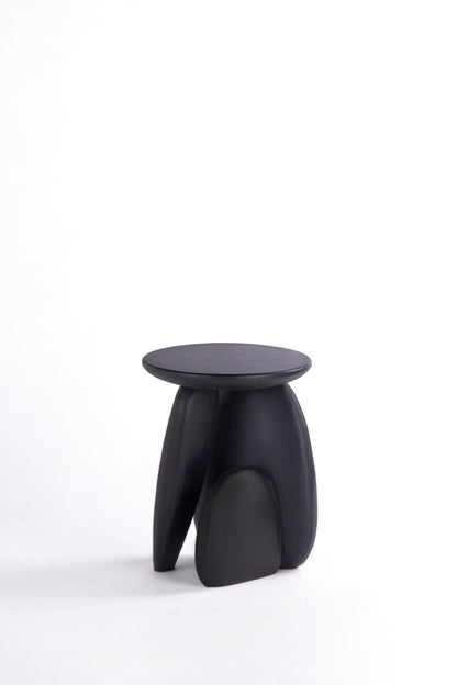 Pebble stool. A minimalist black sculptural stool with a round top and three organic-shaped legs, photographed on a seamless white studio background.