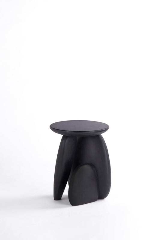 Pebble stool. A minimalist black sculptural stool with a round top and three organic-shaped legs, photographed on a seamless white studio background.