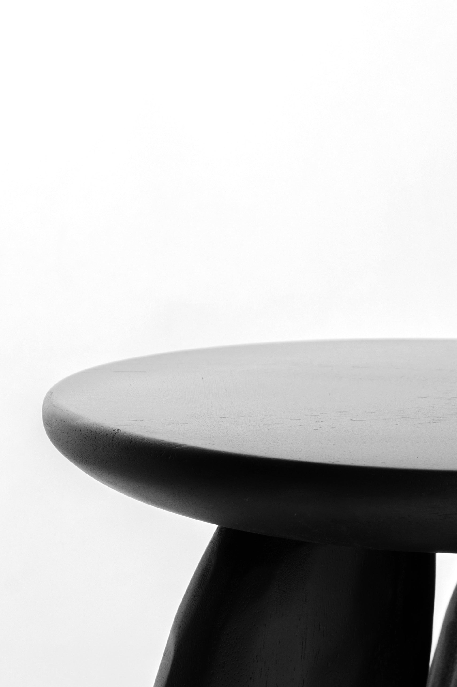 Pebble Stool. A close-up studio shot of a modern black stool with a round top and sculptural curved legs against a plain white background.