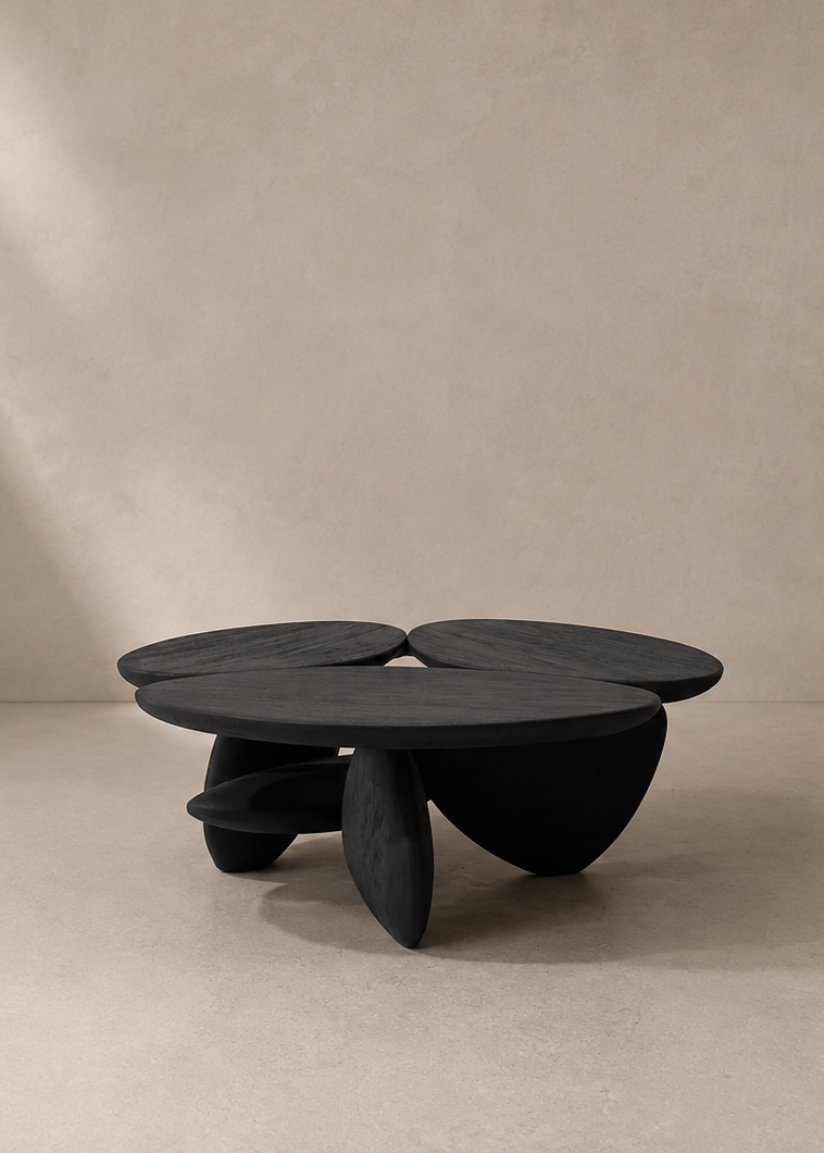 A sculptural black coffee table with a multi-lobed organic shape and thick pedestal legs, set against a minimalist beige textured wall and floor.