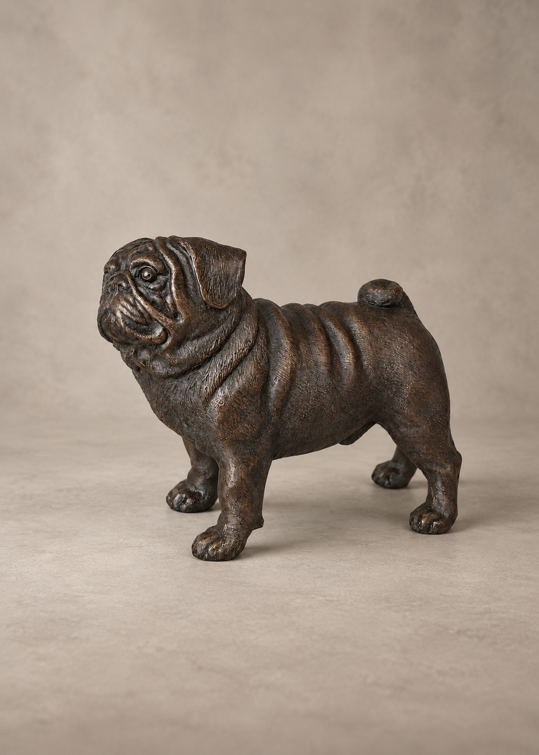 A dark bronze-finished metal sculpture of a pug dog standing in profile, set against a neutral textured beige background.