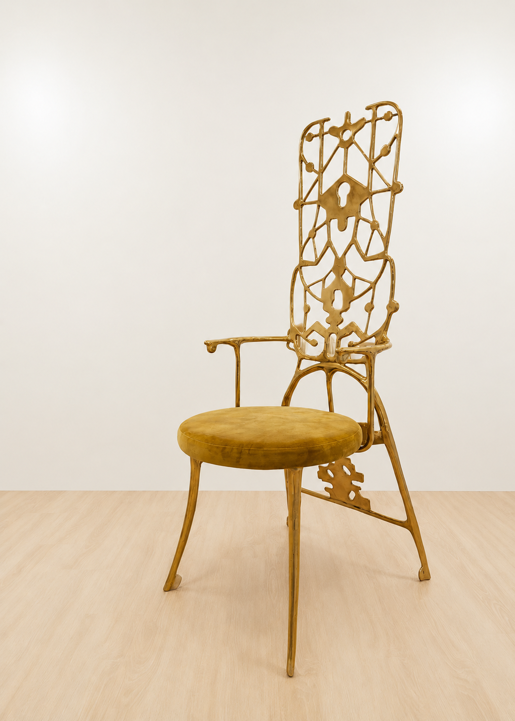 A single decorative chair with a tall openwork brass frame and a round upholstered seat, shown in a minimalist room with a white wall and light wood floor.