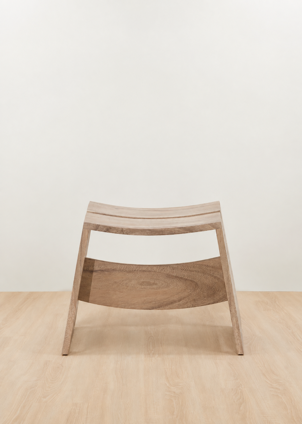 A modern wooden stool with a curved slatted seat and a curved lower support rail, shown in a minimalist studio setting with a light beige wall and pale wood floor.