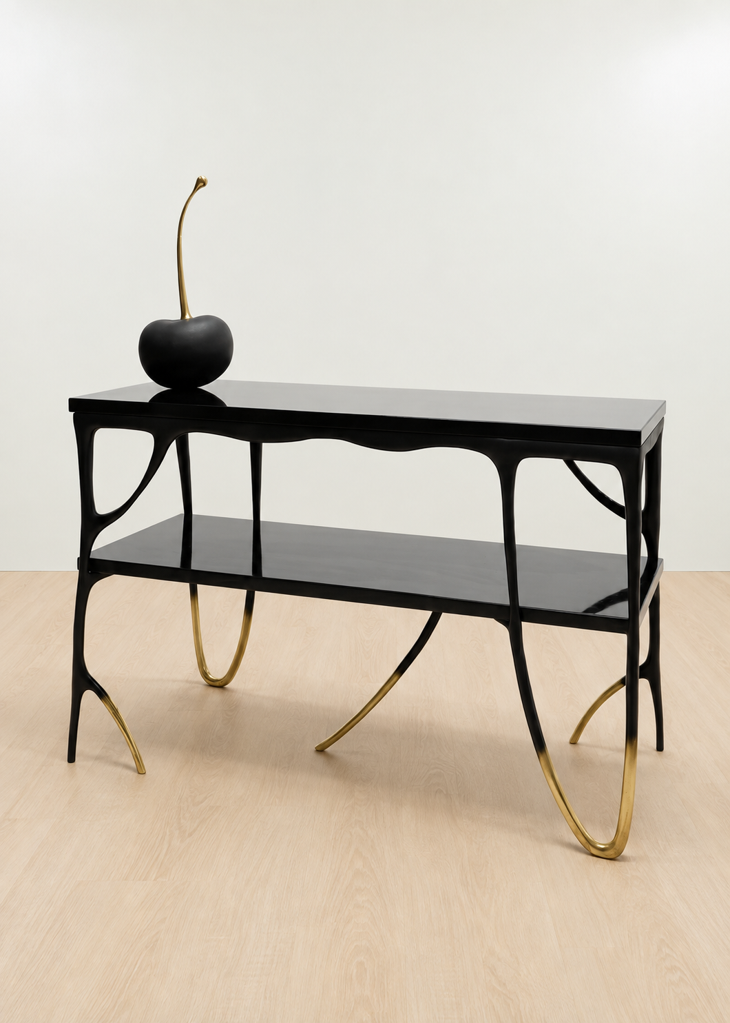 A modern black brass console table with a glossy finish, featuring organic, branching legs with gold-toned metal tips and a lower shelf. A black decorative object with a long gold stem sits on top.