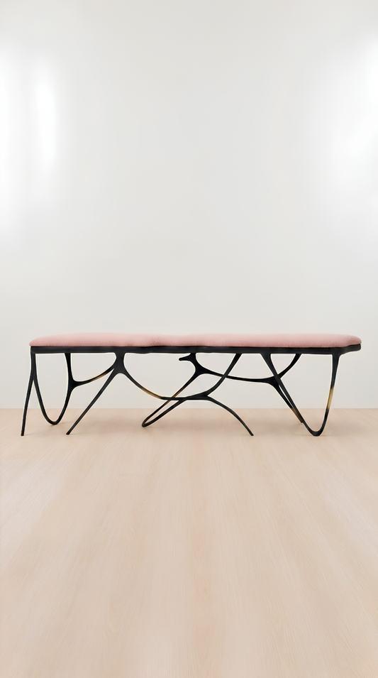 A modern bench with a dusty pink upholstered seat and a sculptural black metal base, shown against a minimalist white wall and light wood floor.
