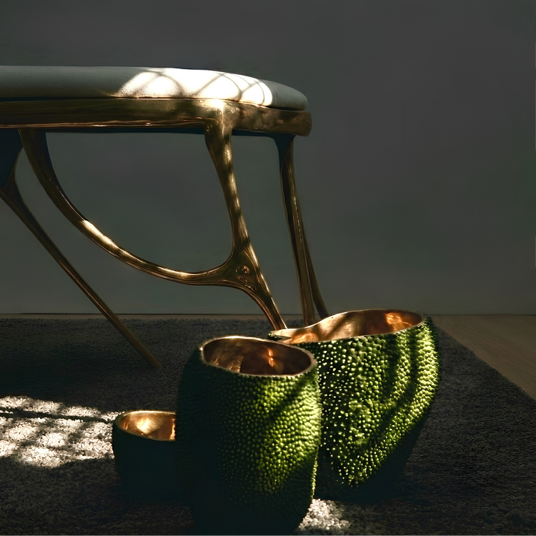 A set of textured green and gold decorative vases arranged on a dark rug in front of a modern gold bench, with dramatic natural light casting shadows across the scene.