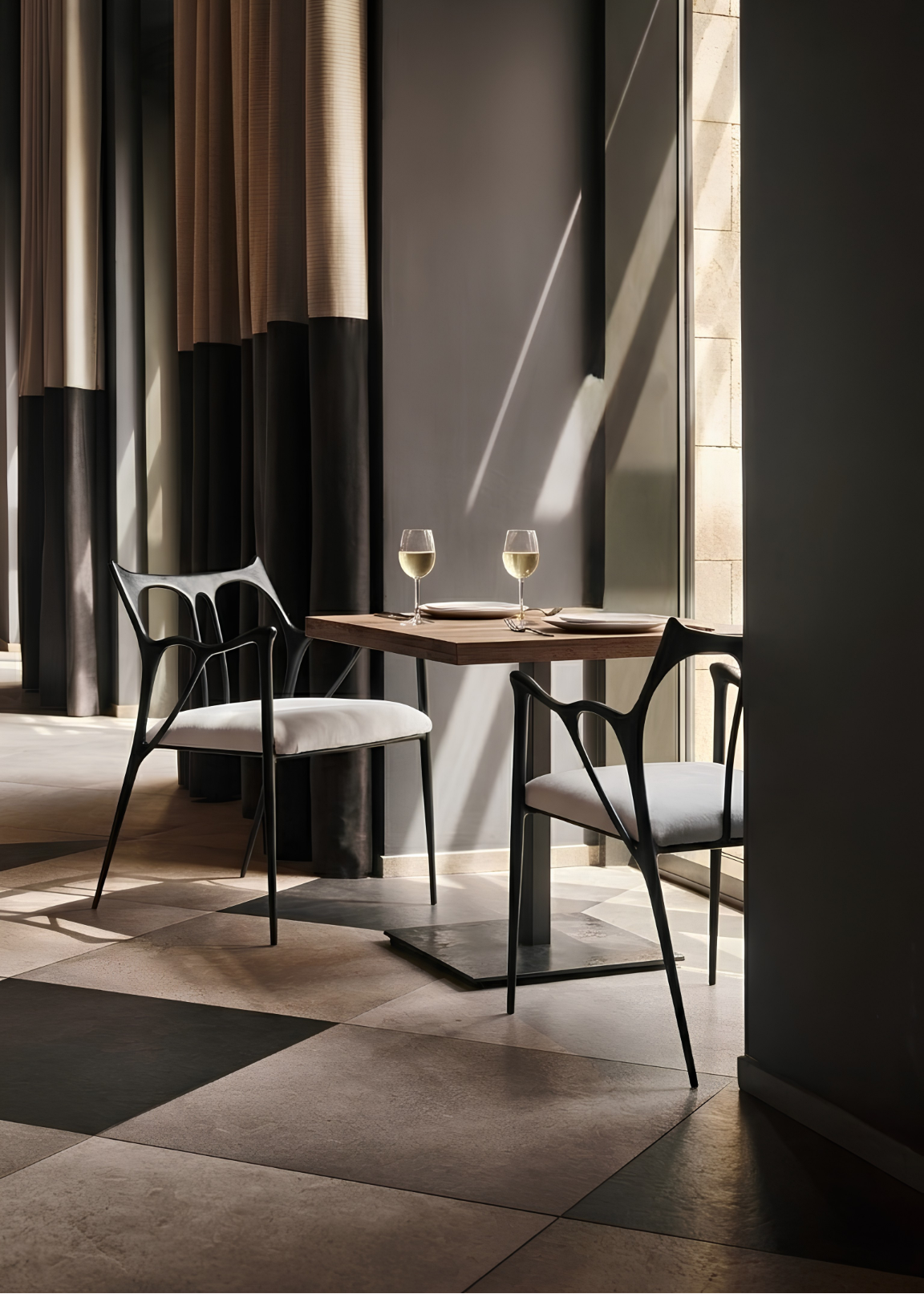 Two black finish Sumi Studio Chairs with light upholstery, and two wine glasses on a dark checkered floor in a stylishly lit interior.